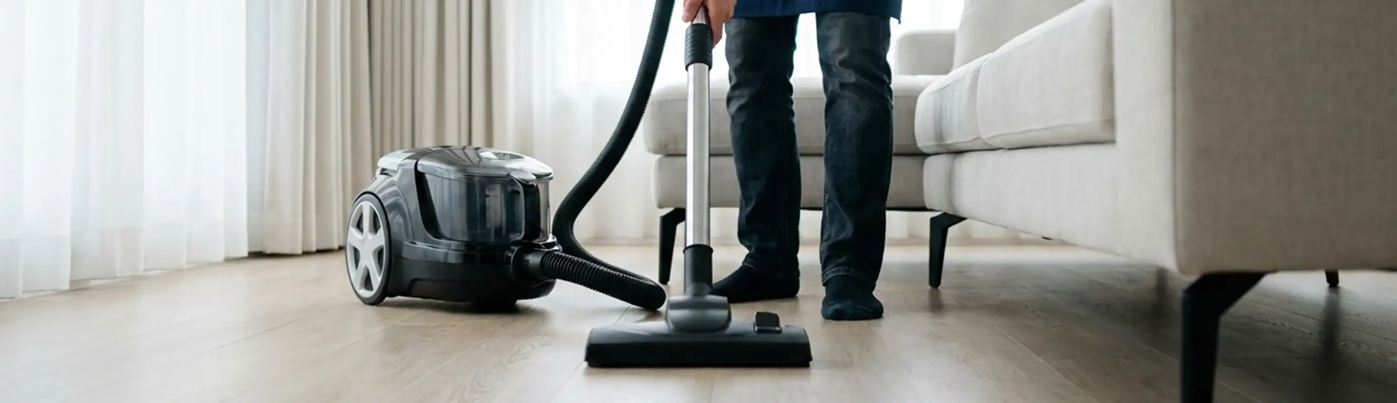Professional house cleaner vacuuming a living room floor with a canister vacuum cleaner, Albany, NY.