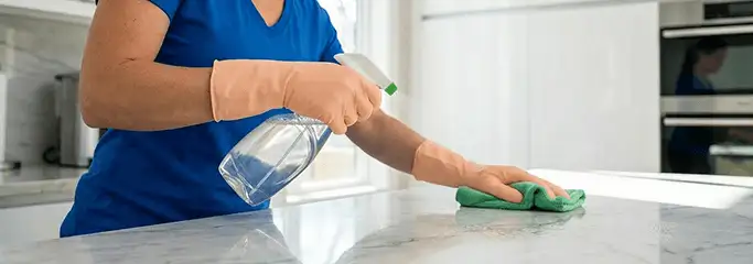 Maid service worker spraying and wiping a kitchen countertop with a microfiber cloth for sanitizing, Albany, NY.