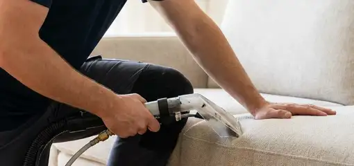 Professional upholstery cleaner deep-cleaning a fabric sofa with a handheld extraction tool, Albany, NY.