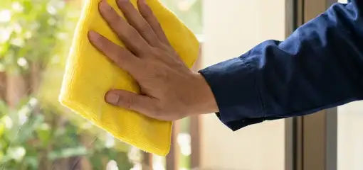 House cleaner wiping a glass window with a yellow microfiber cloth for streak-free cleaning, Albany, NY.
